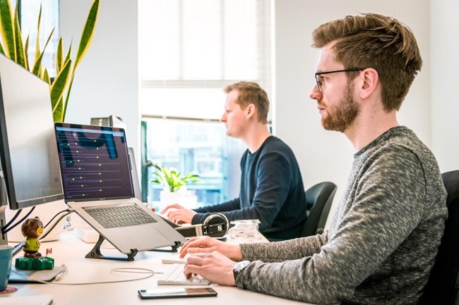 Two men in an office researching sales leadership on their computers